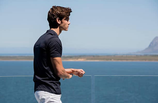 Jeune homme en polo noir et pantalon blanc qui regarde la mer