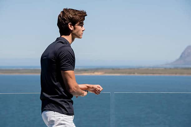 Jeune homme en polo noir et pantalon blanc qui regarde la mer